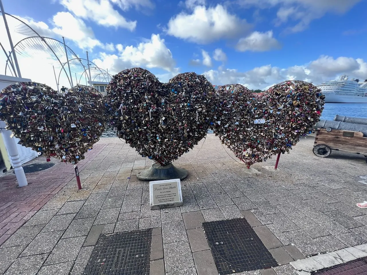 Love lock heart sculptures on Curacao waterfront with cruise ship in background